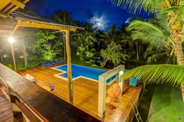Vista do alto, à noite, do deck com pórtico e piscina no Condomínio Txai